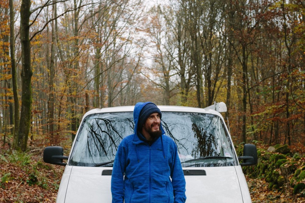 Theo standing in front of his campervan in Soderasen National Park in autumn as the trees have golden leaves